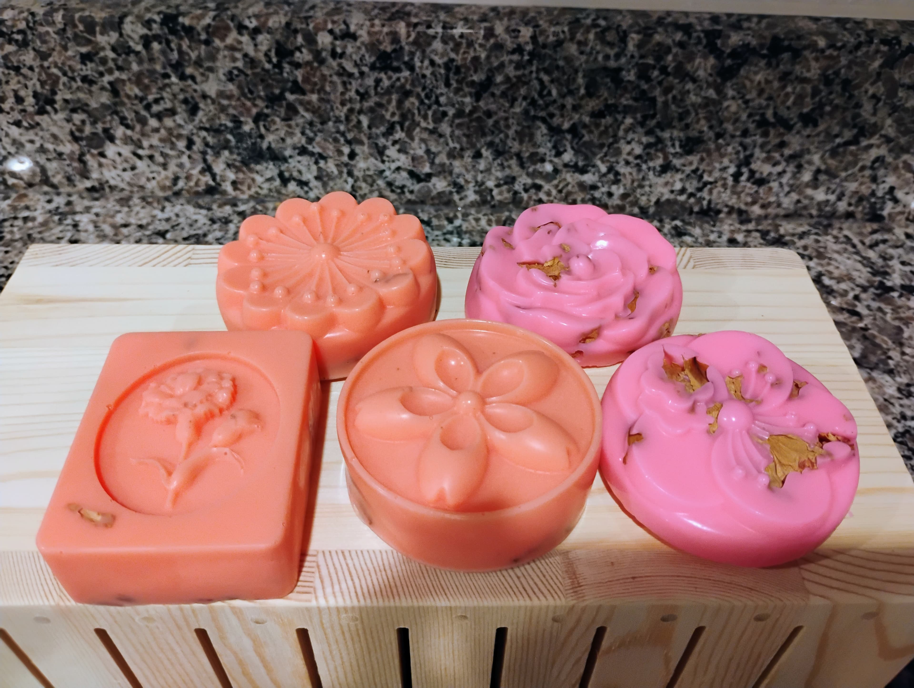 Five peach and pink floral-shaped soaps displayed on a light wooden soap drying rack.