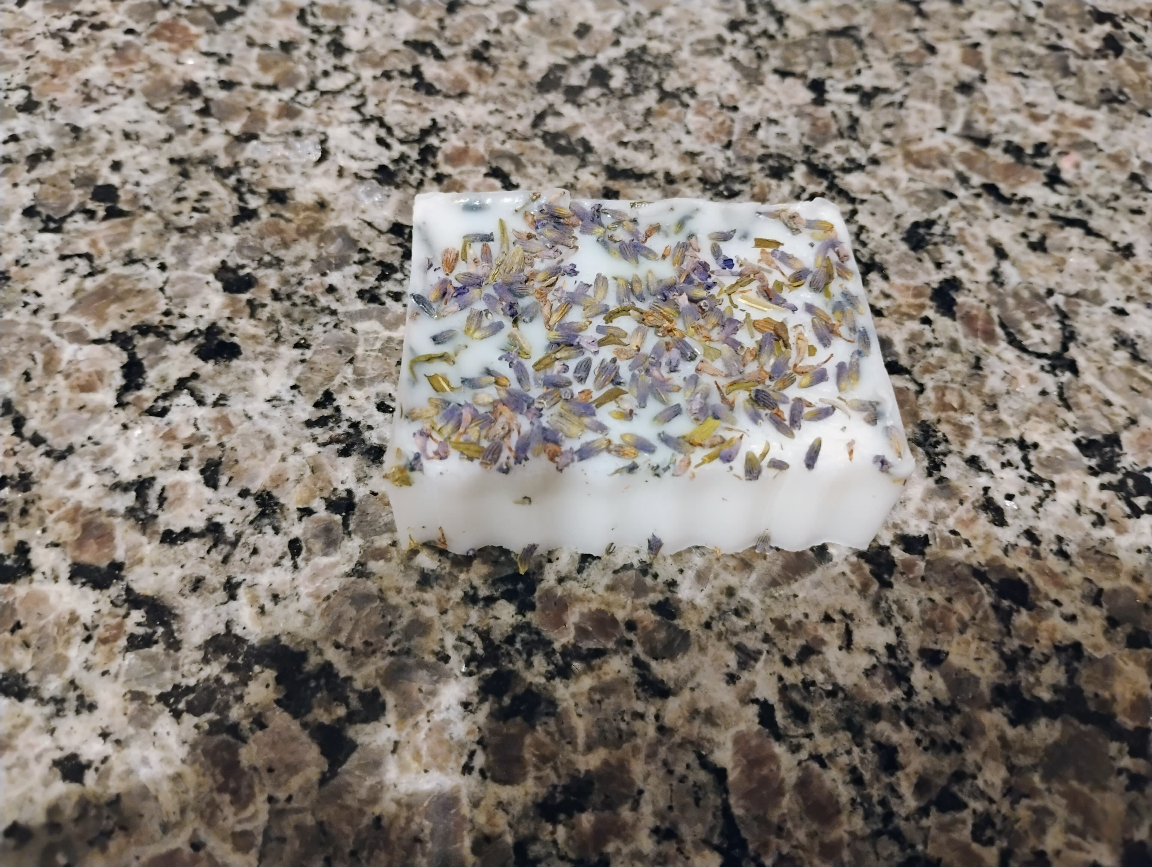 Rectangular white soap bar topped with dried lavender buds on a speckled granite countertop.