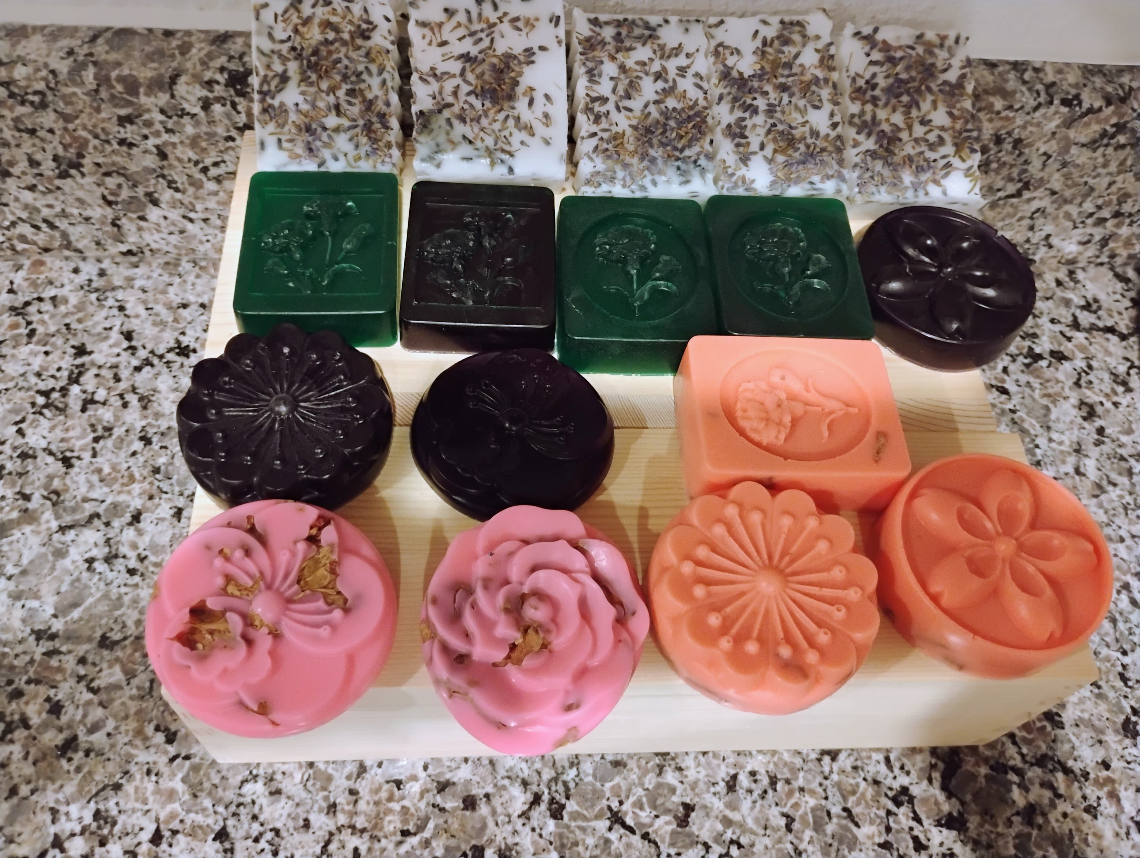 Colorful handmade soaps with floral designs and lavender toppings arranged on a wooden stand.